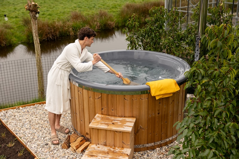 Man in badjas roert met een peddel in een houtgestookte hottub
