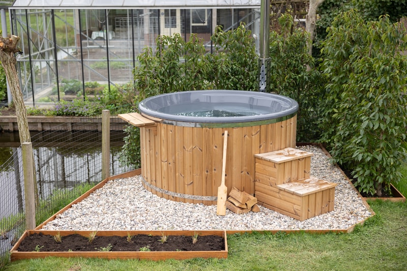 Ronde houtgestookte hottub met trapje en peddel in een tuin