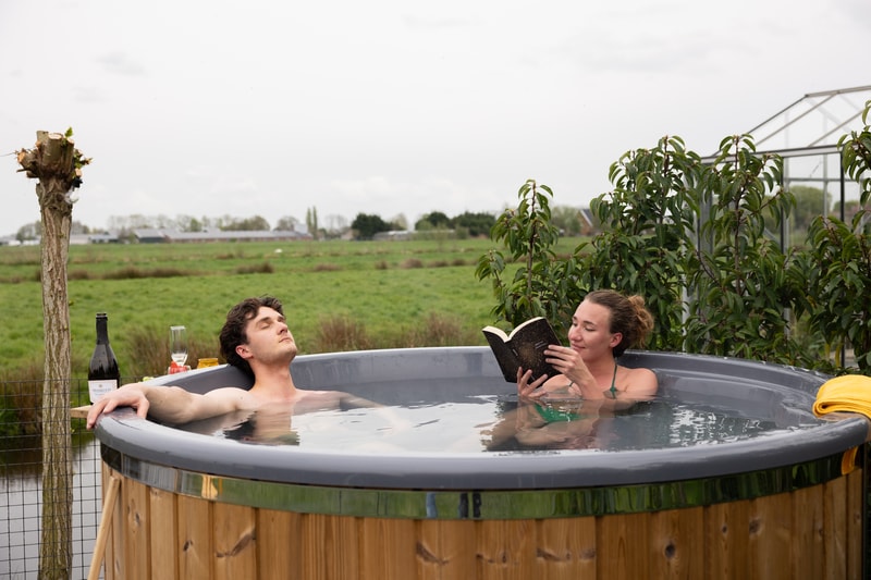 Man en vrouw ontspannen met een boek en een glas in een houtgestookte hottub