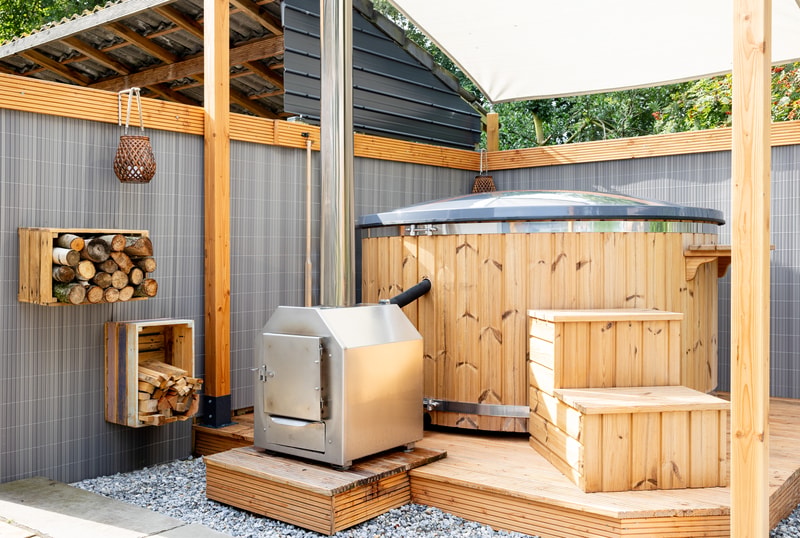 Houtgestookte hottub met externe RVS-kachel en haardhout op een terras